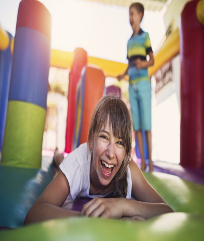 Boy and girl having fun jumping in inflatable castle playground. Sunny summer day